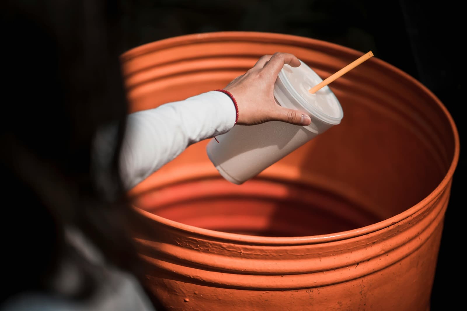 A hand placing a takeout cup into an orange household bin